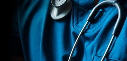 A person wearing blue nursing scrubs with a stethoscope around their neck