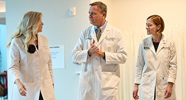 Three AHN doctors talking as they are walking down a hallway in the cancer institute.