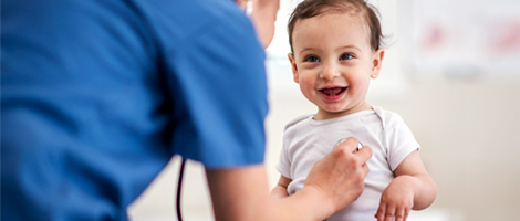 A baby smiling as a pediatrician listens to heart with a stethoscope