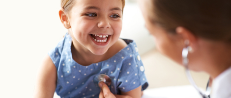 A young girl smiling as a pediatrician listens to her heart with a stethoscope
