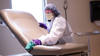 A medical professional cleaning an exam room.