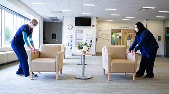 Health care workers separating chairs in a waiting room to have more space in-between them.