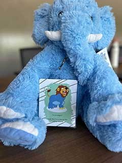 A plush, blue elephant toy holding a greeting card featuring a cartoon lion
