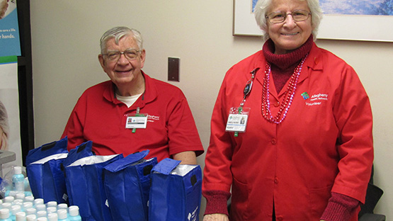 Two AHN volunteers wearing their red AHN volunteer coats standing at a table with water bottles and other supplies.