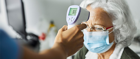 A medical professional taking the temerature of an older woman who is wearing a mask.