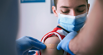 A nurse is placing a band-aid on boy's arm after vaccine shot.