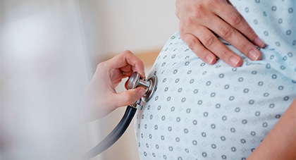 A physician listening to a pregnant women's baby using a stethoscope.