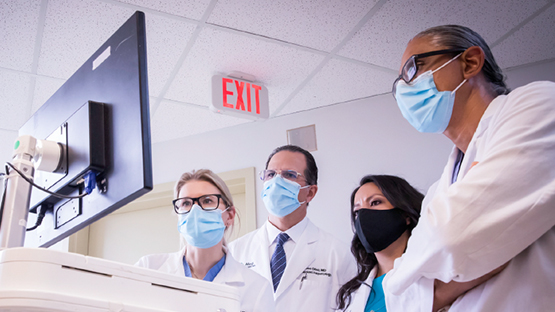Four AHN physicians standing around a monitor and collaborating on a patient's care.