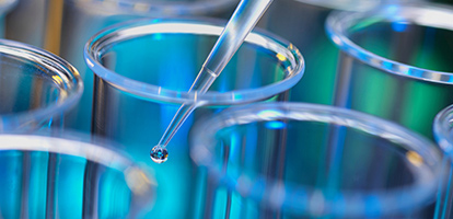 An eye dropper with liquid being placed into a petri dish.