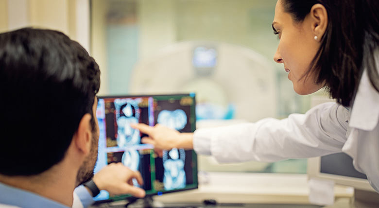 Two medical professionals in white coats look at a computer screen that shows medical images.