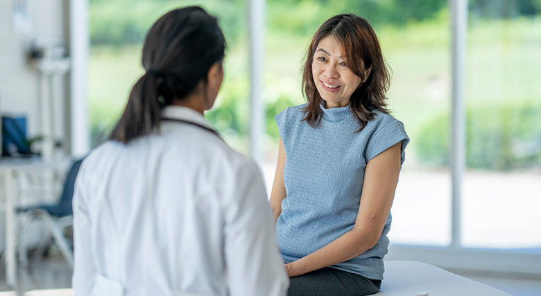 An Asian woman talks to a medical professional in a white coat in a sunny office.