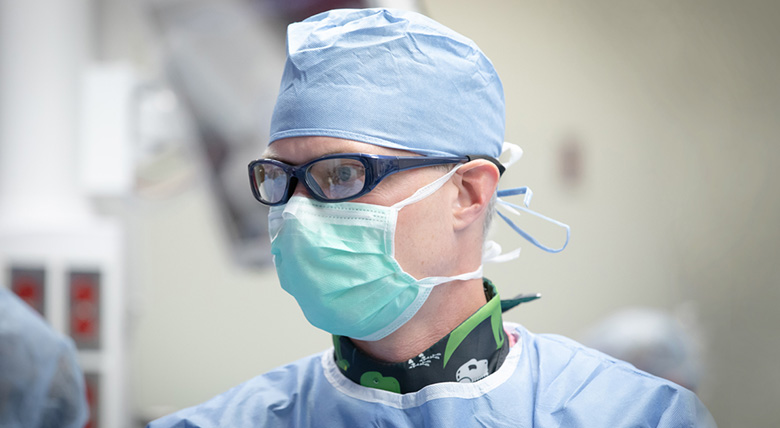 A doctor in blue surgical clothes and a mask is working hard in an operating room.
