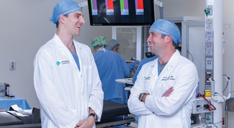 Ryan Sauber, MD, posing with another AHN orthopaedic surgeon in operating room.