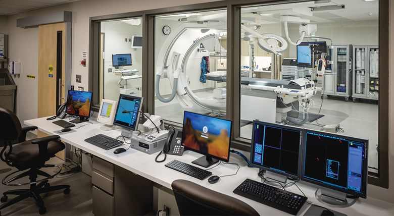 A hospital room has lots of computers and monitors in front of a procedure area.