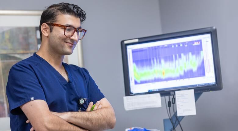 Doctor smiling with his arms crossed with a monitor behind him