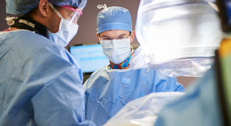 Doctors wearing blue surgical clothes are focused during an operation.
