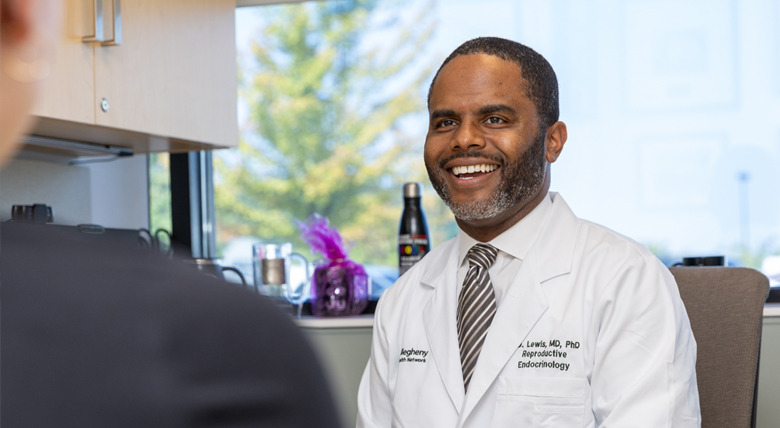 A Black male medical professional in a white coat smiles while talking to a patient.
