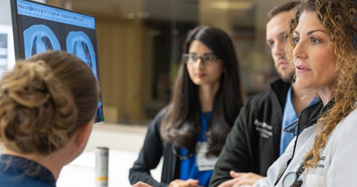 Medical professionals discuss a scan shown on a computer screen.