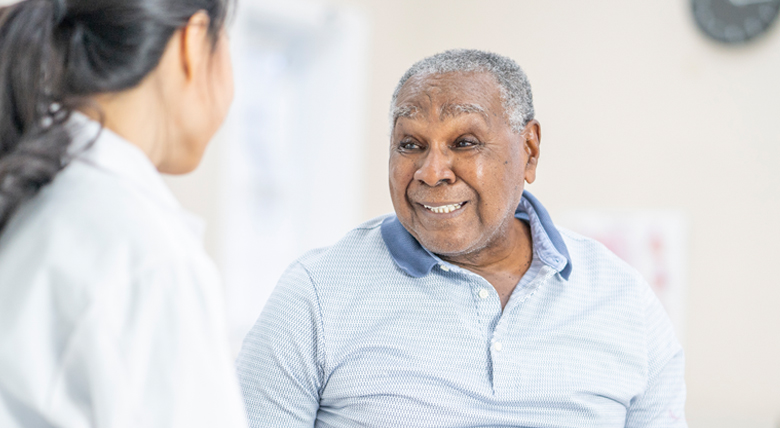A Black man smiles at a medical professional in a white coat.