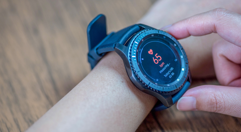 A person checks their smartwatch showing a heart rate of 65 bpm.