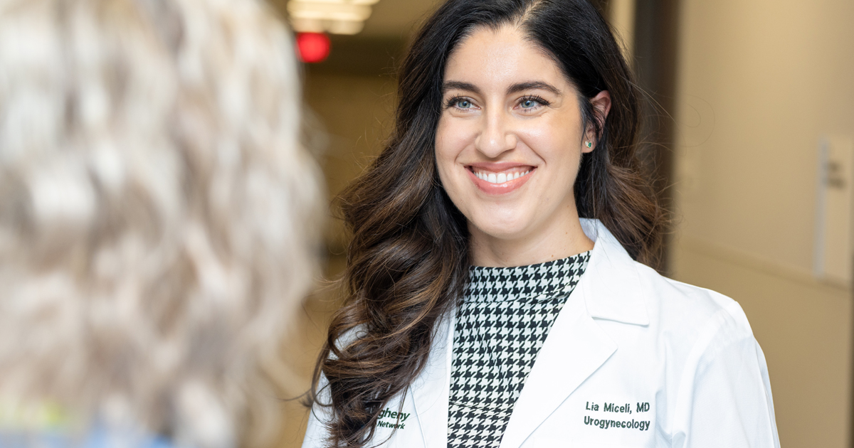A smiling white medical professional in a white coat talks to a patient in a hallway.