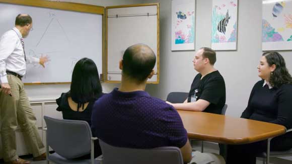 Four child and adolescent psychiatry fellows sit around a conference table, listening to a lecture from faculty.