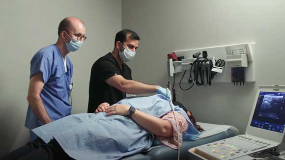 Endocrinology fellow performing an ultrasound of the thyroid under the supervision of an attending physician.