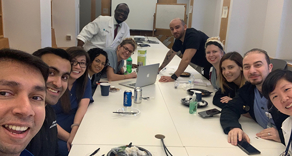 group of people sitting around a conference table with a computer and some food are smiling at the camera