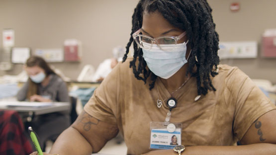 An AHN Schools of Nursing student wearing a mask and glasses, seated at a desk