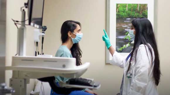 A female neurology resident performs a cranial nerve test, instructing a female patient to visually follow her fingers without moving her head. 