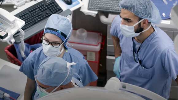 Two thoracic surgeons in training observe faculty during a surgical procedure.