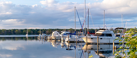 A view of a marina with several boats docked with calm waters and a partially clouded sky.