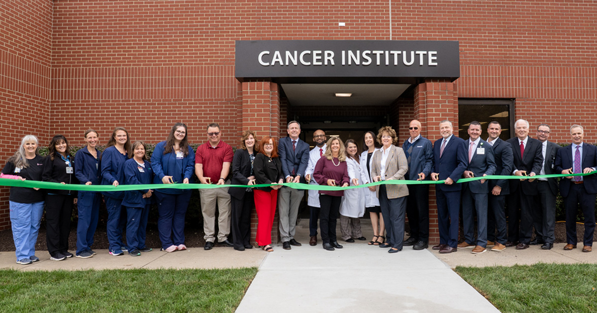 Staff and medical professionals cut a green ribbon at a new medical building.