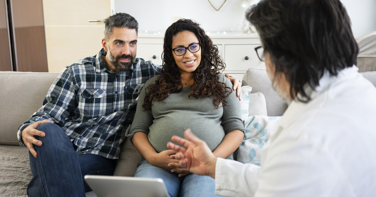 Expectant couple actively engaged in a consultation with a healthcare professional in a clinical setting.