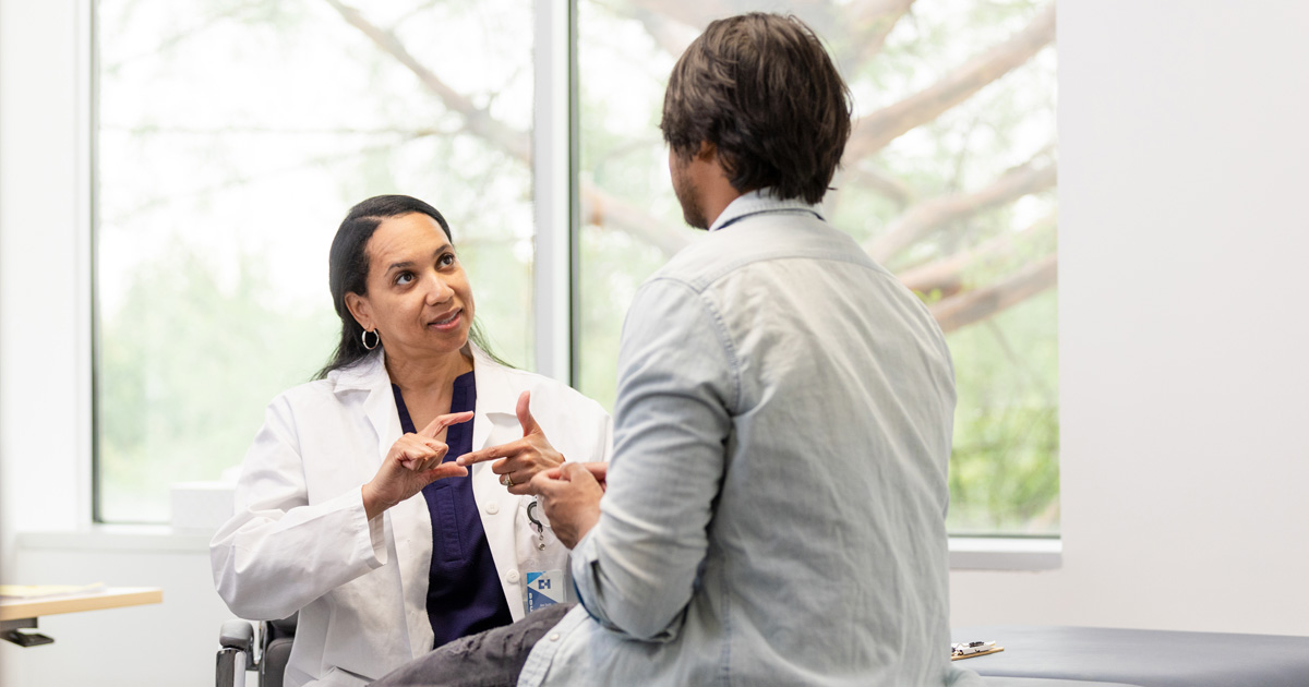 A Latina medical professional in a white coat explains something to a male patient.