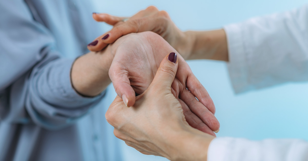 Close-up of a provider gently examining a patient’s hand and wrist, checking for pain or sensitivity, in a clinical setting to diagnose or treat hand conditions like carpal tunnel syndrome.