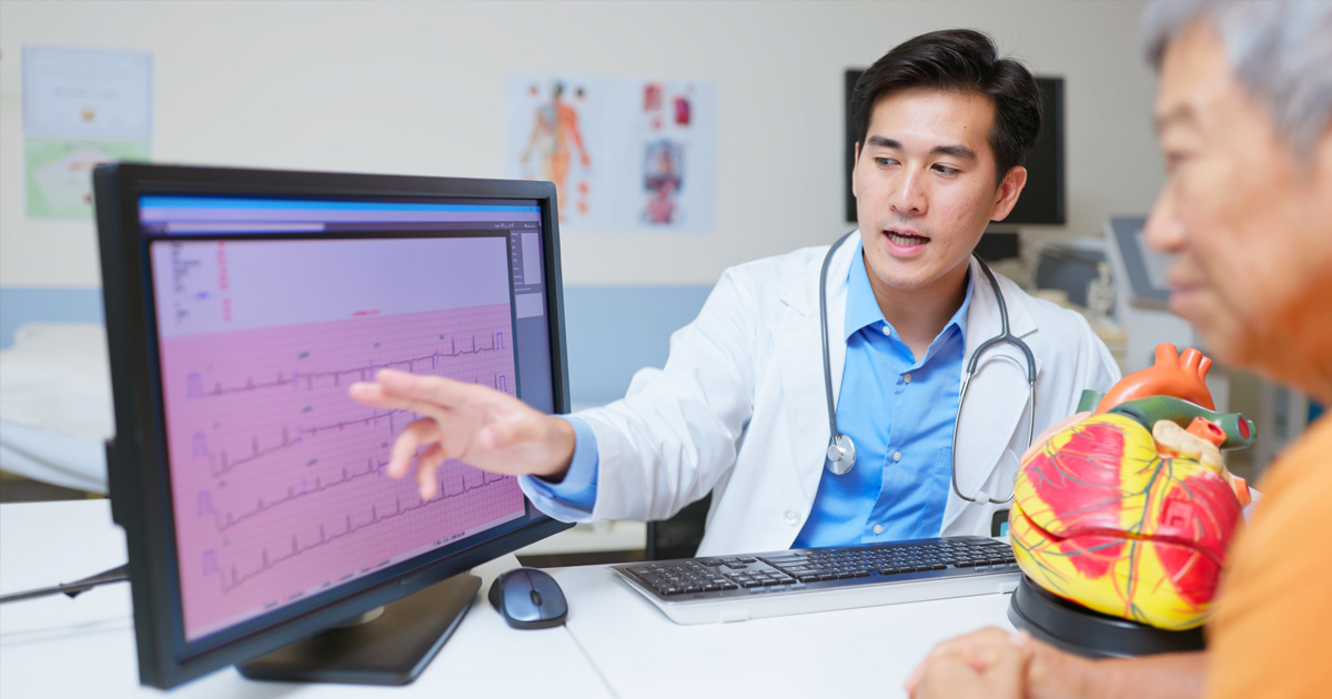 A medical professional in a white coat shows a patient their heart monitor reading.
