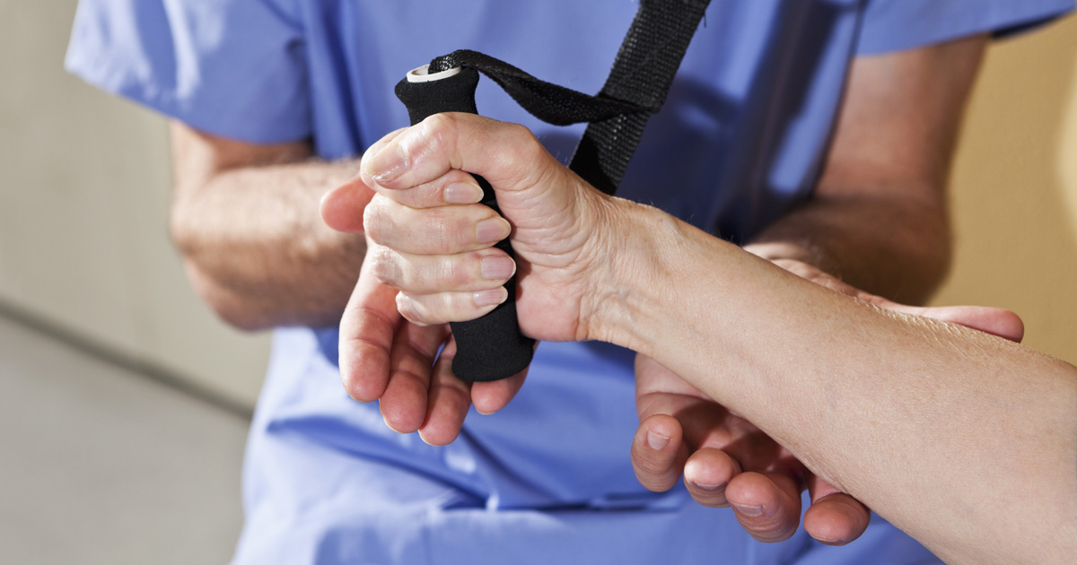 A medical professional in blue scrubs helps a person exercise their hand with a grip.
