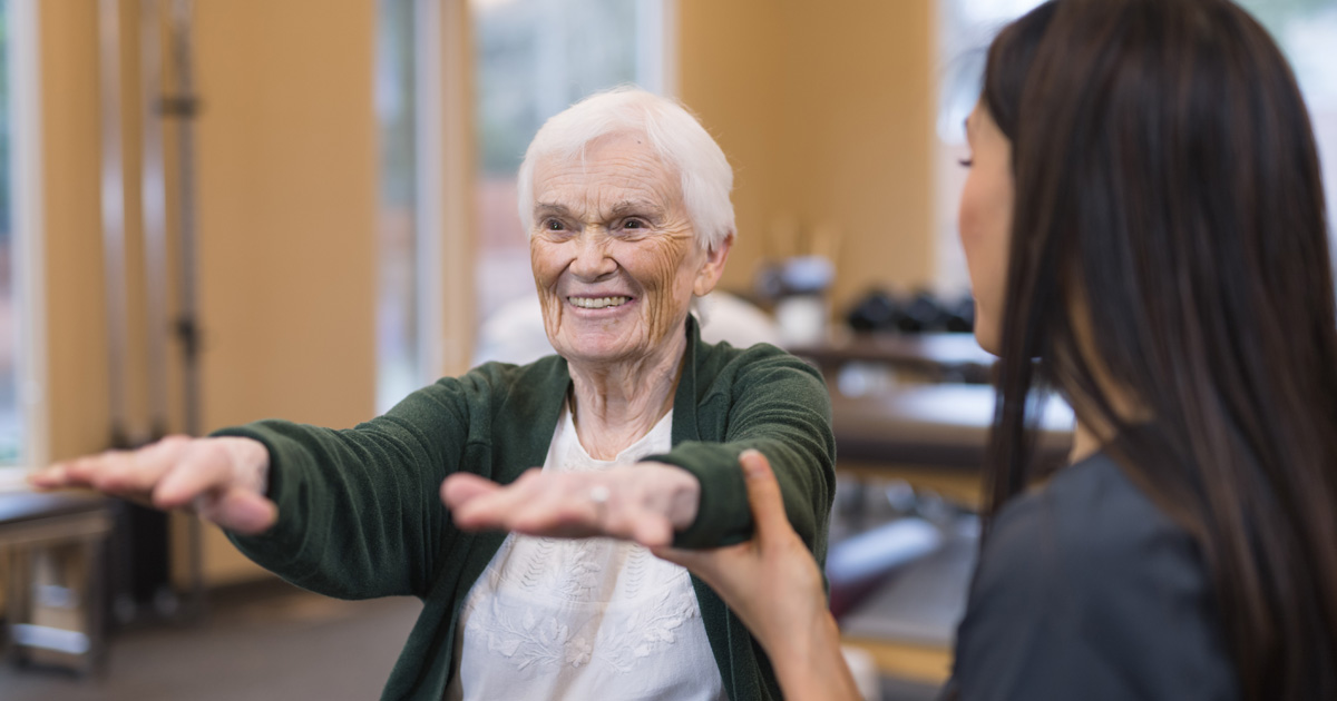 A happy elderly white woman exercises with a medical professional.