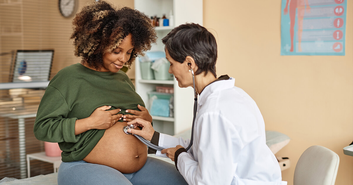 Pregnant woman with doctor listening to her abdomen with stethoscope