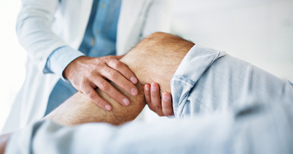 A medical professional in a white coat examines a person's knee.