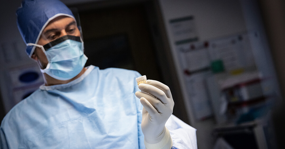 Doctor in operating room scrubs holding replacement heart valve