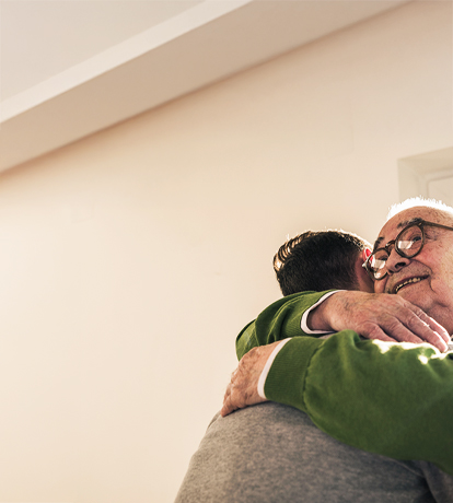 A grandpa with glasses hugs a person with short hair, showing love and connection.