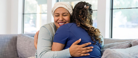 A female patient happily hugs a female healthcare worker on a couch.