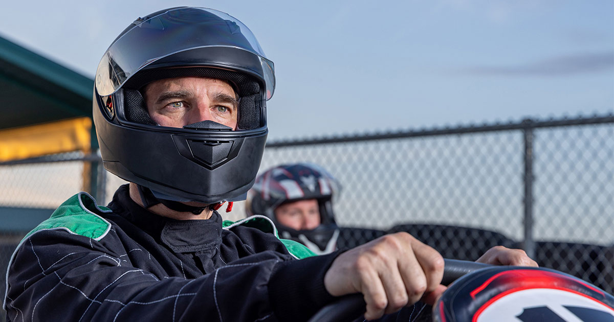 male race car driver in helmet smiling while gripping steering wheel