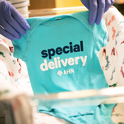 A nurse holding a newborn onesie with the print saying, "special delivery AHN".