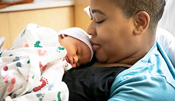 A nurse holding a newborn onesie with the print saying, "special delivery AHN".