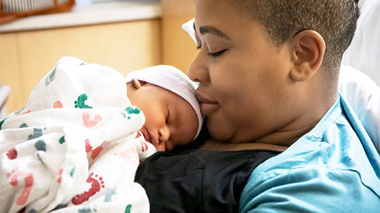 A new mother holding her newborn baby, which is wrapped in a blanket against her chest.