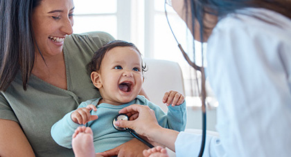 A physician using a stethoscope on a young patient who is being held by the mother.