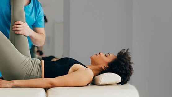 A physician stretching a patient's right leg who is laying on a massage table.